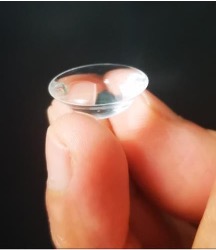 Contact lens resting on top of two pinched fingers