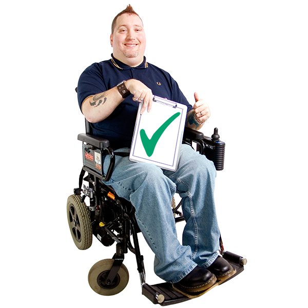 Person sitting in an electric wheelchair, holding a white card with a green tick in their right hand and their left hand has a thumbs up.