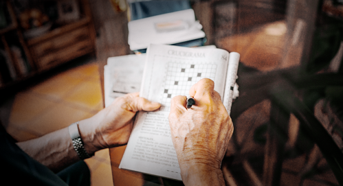 An over-shoulder view of a person's hands completing a crossword book