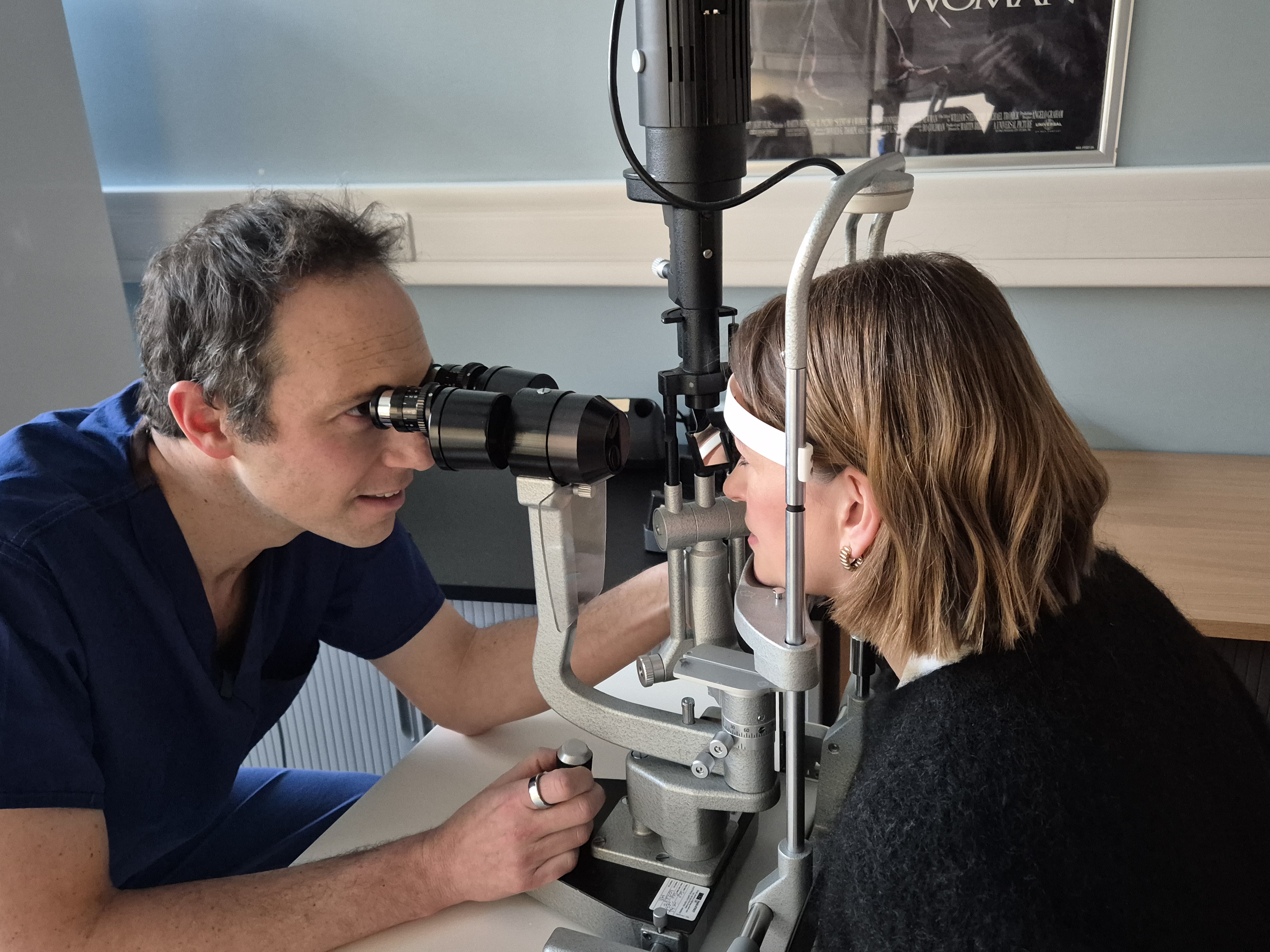 Patient with their head resting against examination equipment with consultant looking in their eye. 