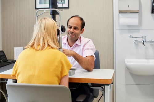 Consultant performing an Eye Examination and smiling at a patient in a yellow top