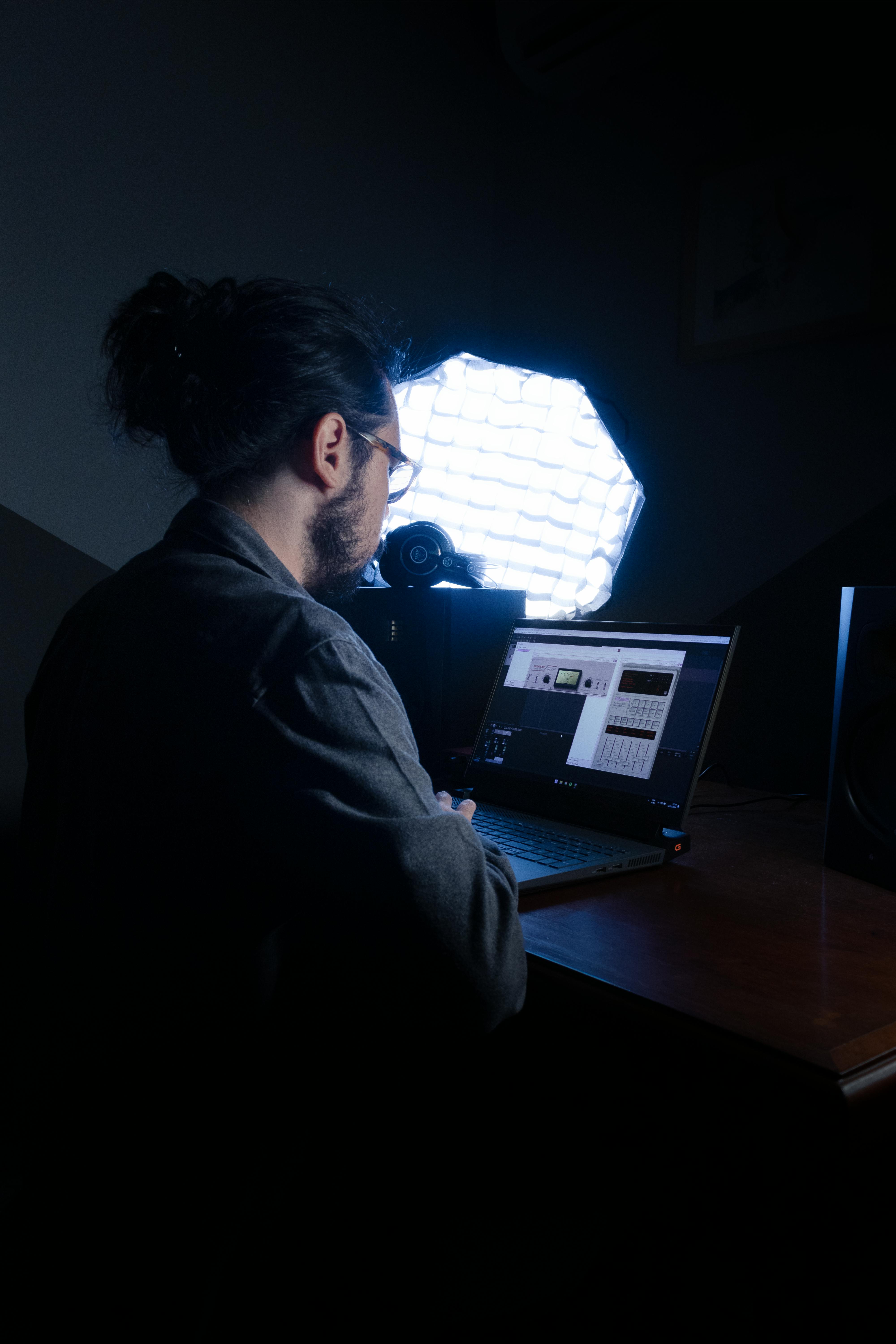 Person in a dark room with one octagon spotlight looking at computer screens