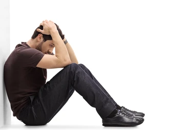 Side view of a person sitting on the floor with their elbows on their knees and their head in their hands