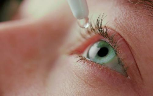 Eye drops being inserted into a blue eye